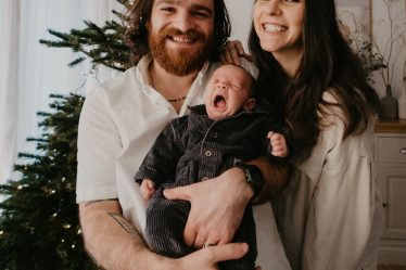 a man and woman holding a baby in front of a christmas tree