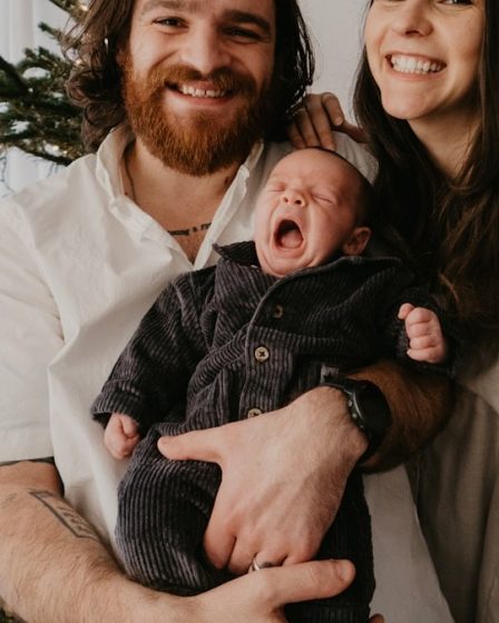 a man and woman holding a baby in front of a christmas tree