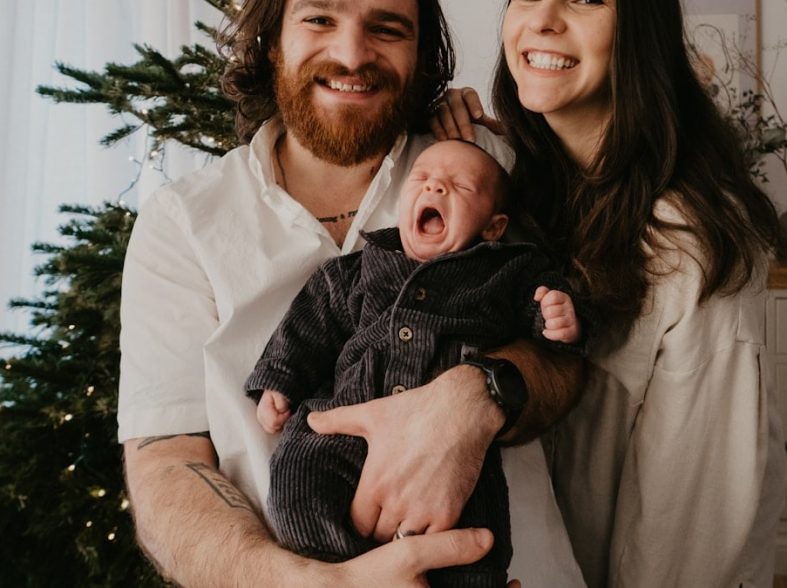 a man and woman holding a baby in front of a christmas tree